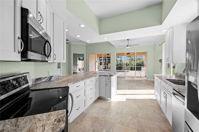 kitchen featuring kitchen peninsula, appliances with stainless steel finishes, light stone countertops, white cabinets, and sink