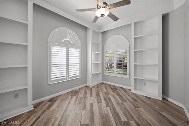 empty room with ceiling fan, built in shelves, hardwood / wood-style flooring, and crown molding