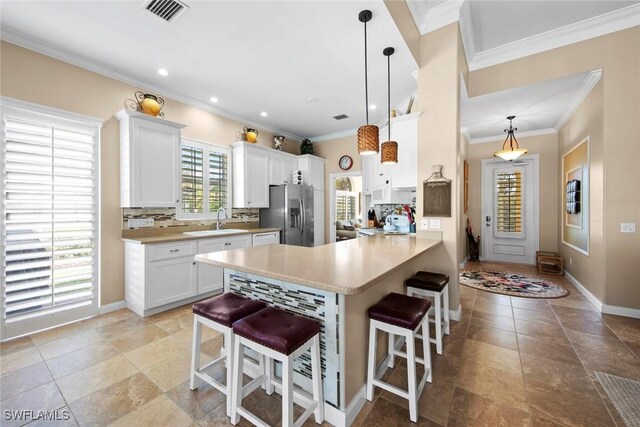 kitchen with hanging light fixtures, kitchen peninsula, stainless steel fridge, a breakfast bar, and white cabinets