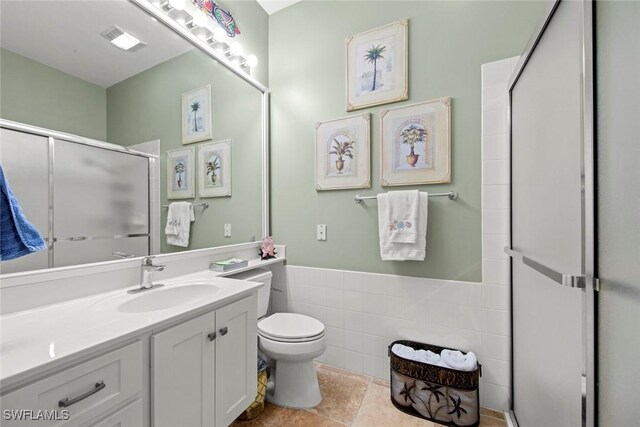 bathroom with tile walls, toilet, tile patterned floors, an enclosed shower, and vanity