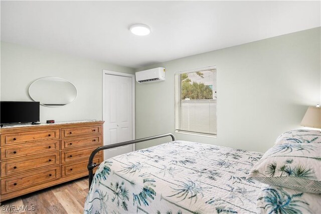 bedroom with a wall mounted AC, a closet, and light hardwood / wood-style floors