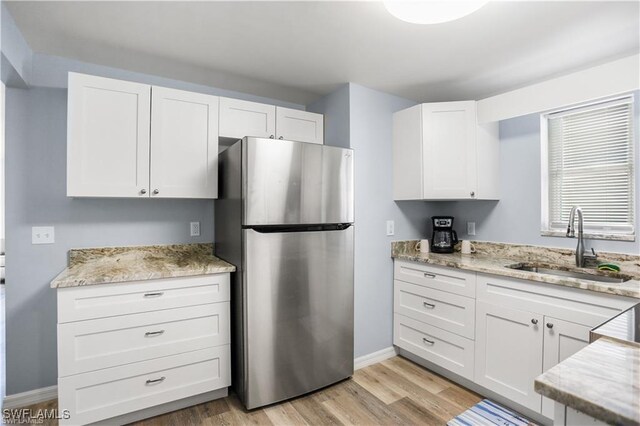 kitchen featuring light stone counters, sink, white cabinets, light hardwood / wood-style floors, and stainless steel refrigerator