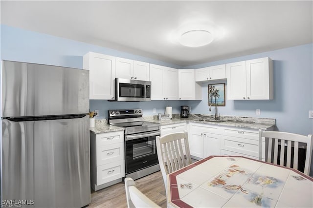 kitchen featuring sink, light stone countertops, light wood-type flooring, appliances with stainless steel finishes, and white cabinetry