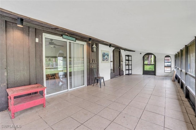 interior space with light tile patterned floors, ceiling fan, and wooden walls