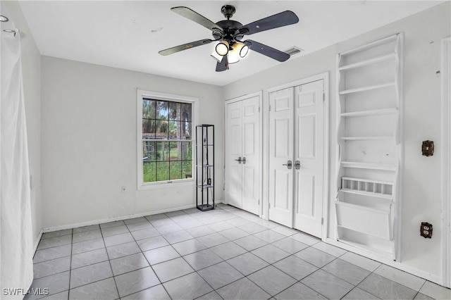 unfurnished bedroom with ceiling fan, light tile patterned flooring, and two closets