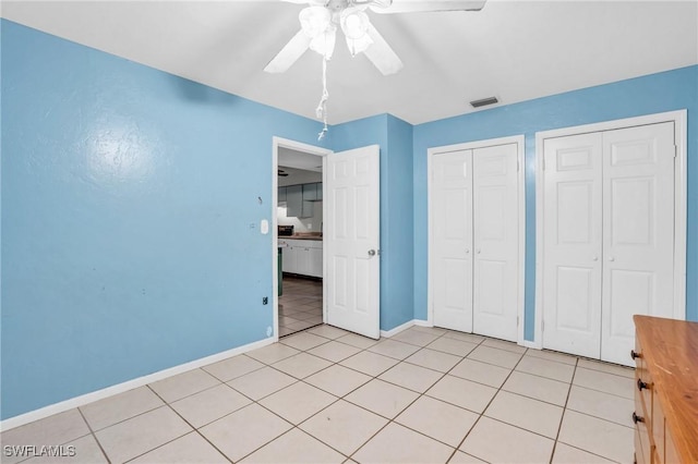 unfurnished bedroom featuring multiple closets, ceiling fan, and light tile patterned floors