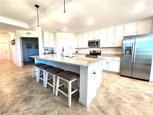 kitchen with hanging light fixtures, appliances with stainless steel finishes, white cabinetry, light stone counters, and a center island with sink