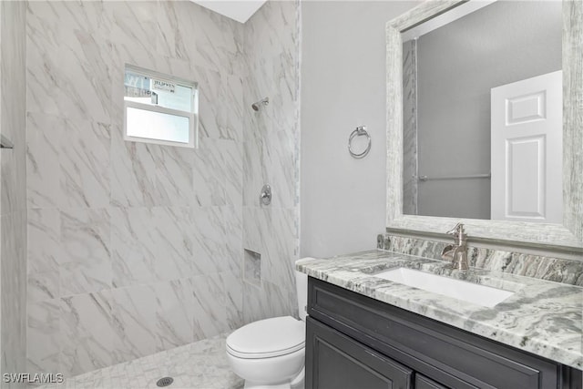 bathroom featuring toilet, tiled shower, and vanity