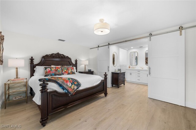 bedroom featuring connected bathroom, a barn door, and light wood-type flooring