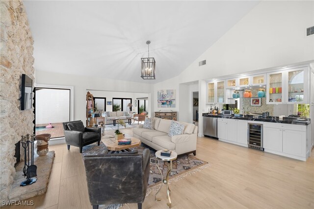 living room with bar, high vaulted ceiling, a fireplace, light hardwood / wood-style floors, and beverage cooler