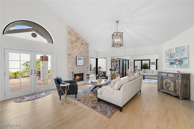 living room featuring a chandelier, french doors, light hardwood / wood-style floors, high vaulted ceiling, and a fireplace