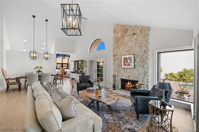 living room with a stone fireplace, light wood-type flooring, high vaulted ceiling, and a chandelier