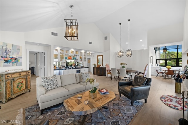 living room featuring an inviting chandelier, high vaulted ceiling, and light hardwood / wood-style flooring