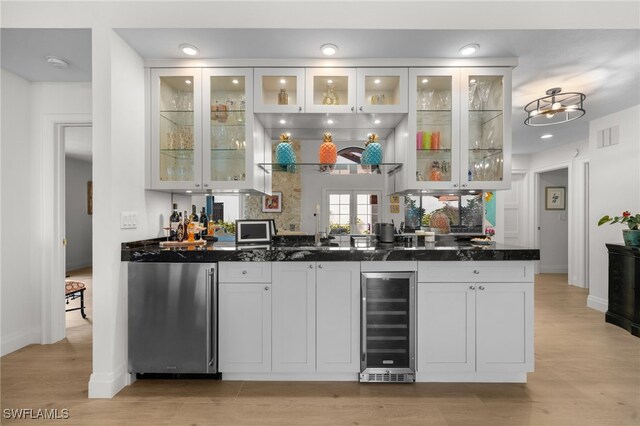 bar featuring light hardwood / wood-style flooring, white cabinetry, dark stone countertops, fridge, and beverage cooler