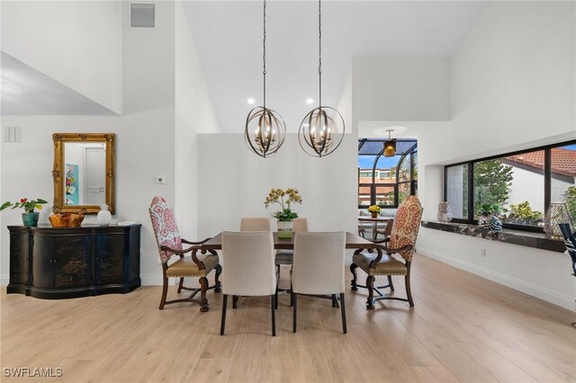 dining space with a towering ceiling, a notable chandelier, and light hardwood / wood-style flooring