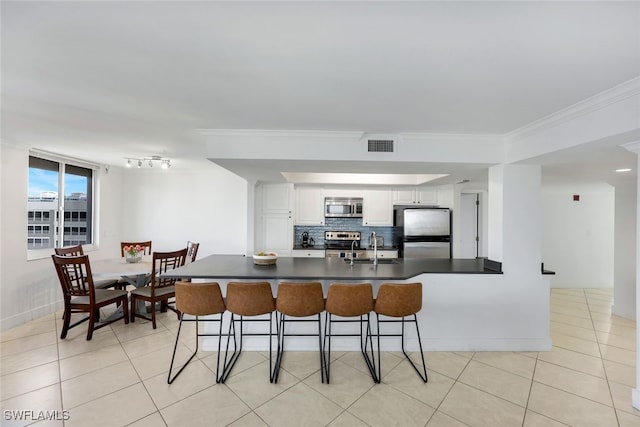 kitchen featuring a breakfast bar area, white cabinetry, tasteful backsplash, light tile patterned floors, and stainless steel appliances