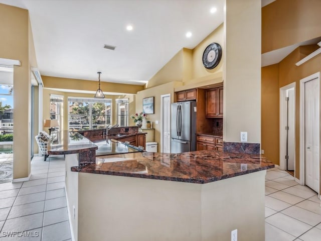 kitchen featuring kitchen peninsula, stainless steel fridge, dark stone counters, hanging light fixtures, and light tile patterned flooring