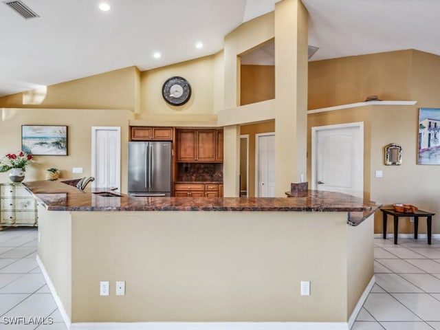 kitchen with sink, dark stone countertops, stainless steel fridge, decorative backsplash, and light tile patterned flooring