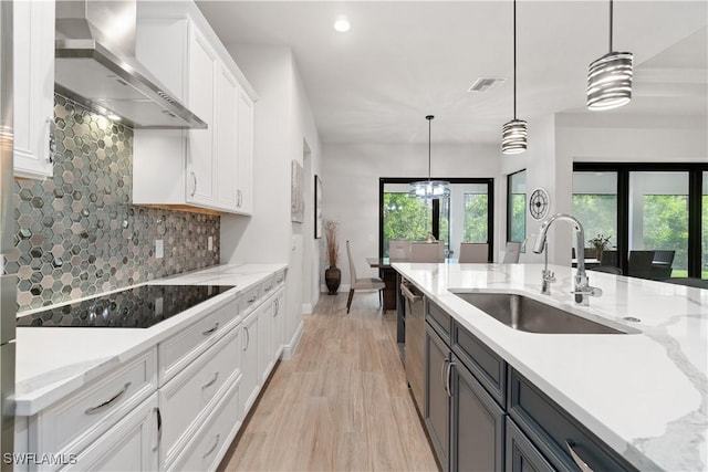 kitchen with backsplash, wall chimney range hood, pendant lighting, sink, and white cabinets