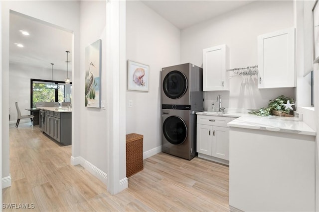 clothes washing area featuring cabinets, sink, light hardwood / wood-style flooring, and stacked washing maching and dryer