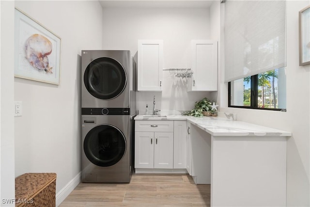 laundry area with stacked washer / drying machine, light wood-type flooring, sink, and cabinets