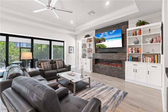 living room featuring ceiling fan, built in features, a fireplace, and a raised ceiling