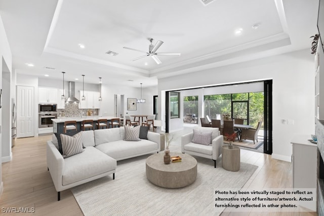 living room featuring ceiling fan, light hardwood / wood-style flooring, and a tray ceiling