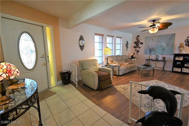 living room featuring ceiling fan, a textured ceiling, beamed ceiling, and light wood-type flooring