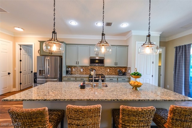 kitchen featuring light stone counters, decorative light fixtures, stainless steel appliances, and an island with sink