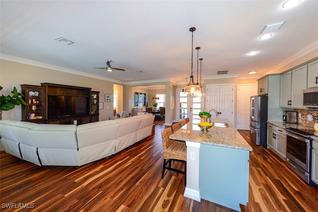 kitchen with a breakfast bar area, a center island with sink, pendant lighting, stainless steel appliances, and light stone countertops