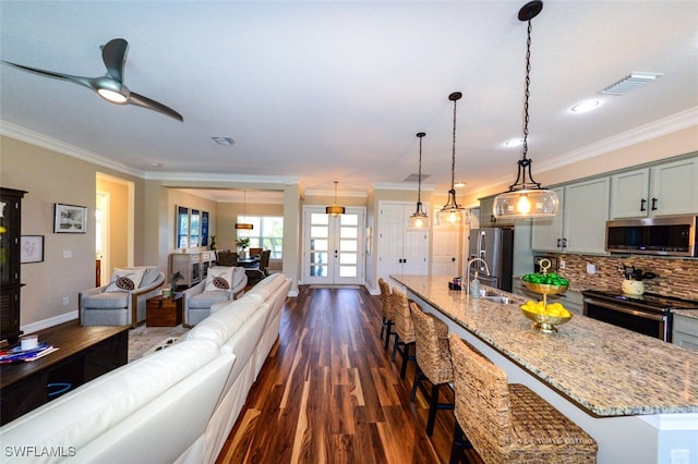 kitchen with pendant lighting, sink, appliances with stainless steel finishes, light stone counters, and an island with sink