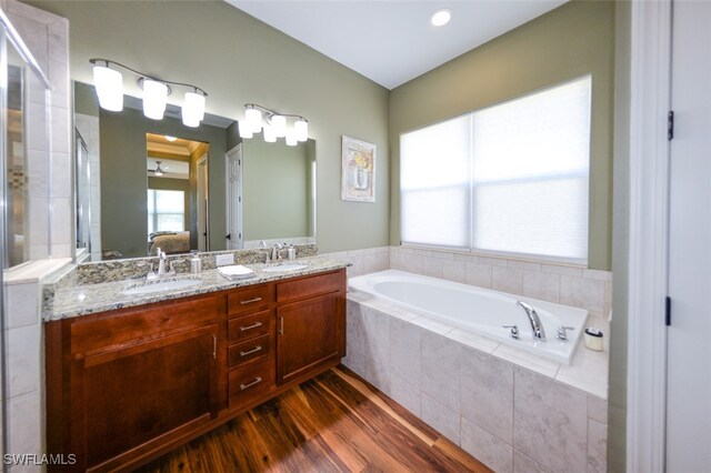 bathroom with hardwood / wood-style flooring, vanity, and tiled tub