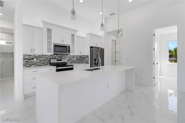 kitchen with white cabinets, pendant lighting, stainless steel appliances, and a kitchen island with sink