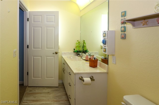 bathroom with wood-type flooring, lofted ceiling, vanity, and toilet