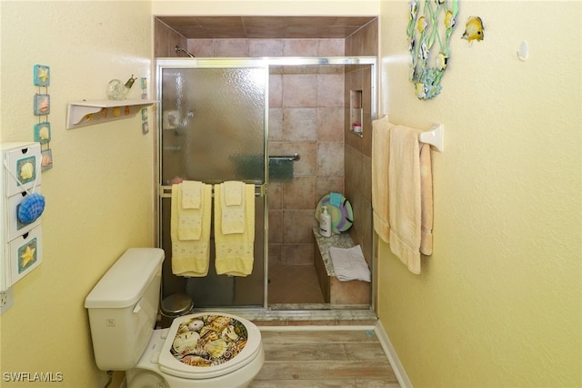 bathroom with hardwood / wood-style flooring, a shower with shower door, and toilet