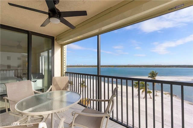 sunroom with ceiling fan, a water view, and a view of the beach