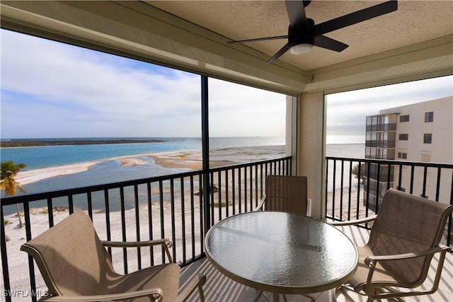 balcony featuring a beach view, ceiling fan, and a water view