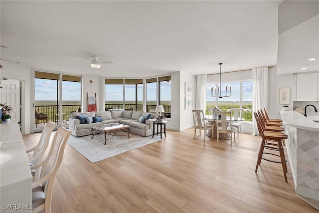 living room with ceiling fan with notable chandelier, plenty of natural light, and light hardwood / wood-style floors