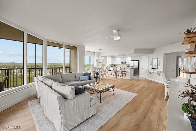 living room with light wood-type flooring, ceiling fan with notable chandelier, and a wealth of natural light