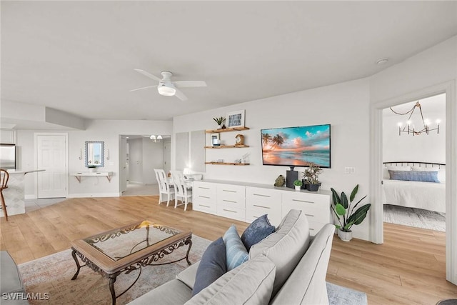 living room featuring ceiling fan with notable chandelier and light wood-type flooring