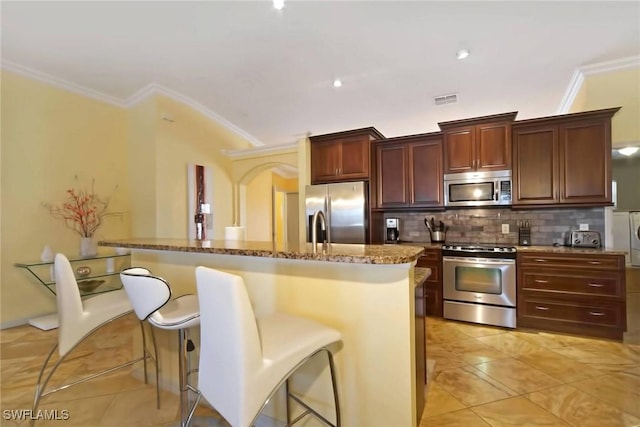 kitchen with an island with sink, appliances with stainless steel finishes, tasteful backsplash, light tile patterned flooring, and a breakfast bar area