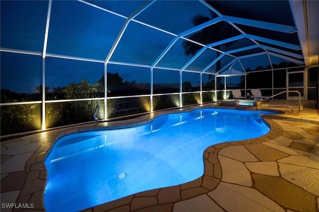 pool at night with a hot tub, glass enclosure, and a patio area