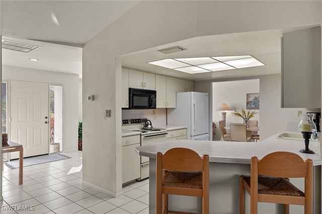 kitchen featuring a kitchen bar, sink, kitchen peninsula, white appliances, and decorative backsplash