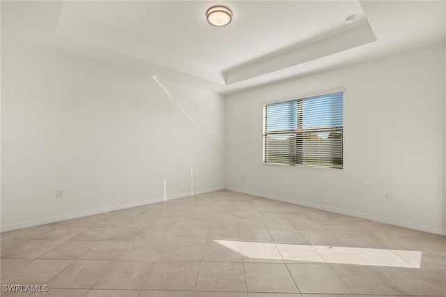 unfurnished room with light tile patterned floors and a tray ceiling