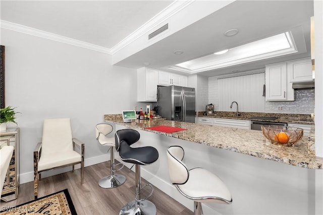 kitchen featuring a kitchen bar, sink, light stone counters, white cabinetry, and stainless steel appliances