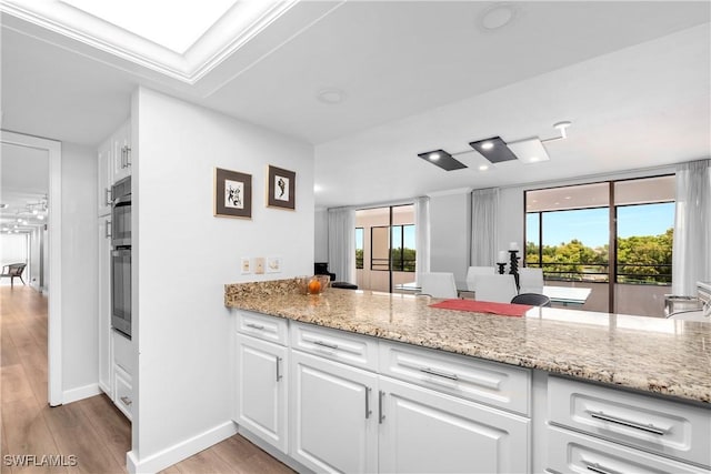 kitchen with white cabinets, plenty of natural light, light stone counters, and kitchen peninsula