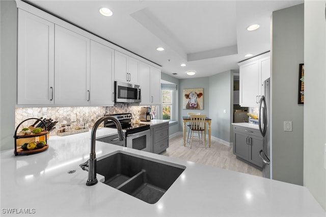 kitchen with a sink, stainless steel appliances, light countertops, and white cabinets