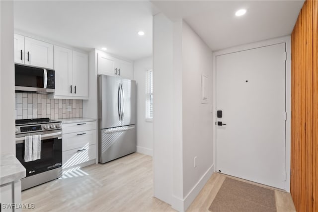 kitchen with stainless steel appliances, white cabinetry, light hardwood / wood-style flooring, backsplash, and light stone countertops