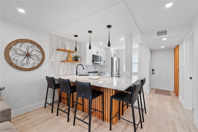 kitchen featuring kitchen peninsula, pendant lighting, stainless steel appliances, tasteful backsplash, and white cabinets