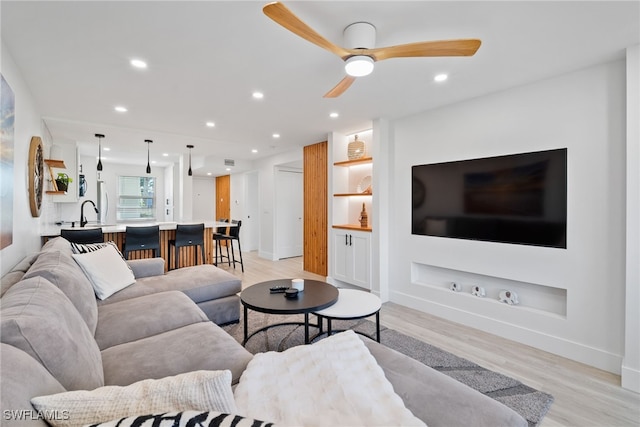 living room featuring light wood-type flooring, built in features, and ceiling fan